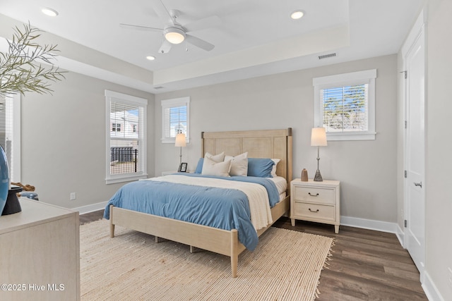 bedroom with multiple windows, dark wood-style flooring, baseboards, a tray ceiling, and recessed lighting