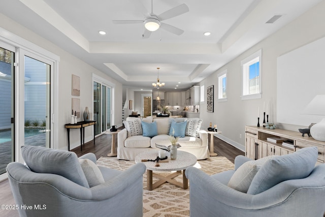 living area with a tray ceiling, baseboards, dark wood-type flooring, a chandelier, and a ceiling fan
