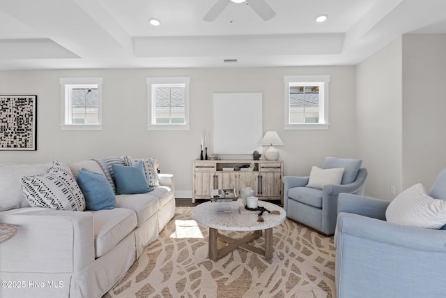 living area with a tray ceiling, plenty of natural light, a ceiling fan, and recessed lighting
