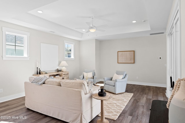 living room with a tray ceiling, a ceiling fan, dark wood-style flooring, recessed lighting, and baseboards