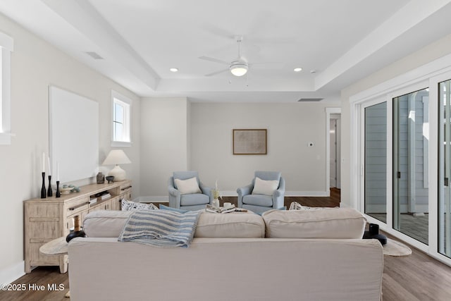 living area featuring a tray ceiling, dark wood-style flooring, a ceiling fan, recessed lighting, and baseboards