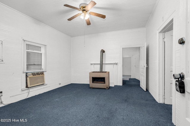 empty room with dark colored carpet, a wood stove, a ceiling fan, heating unit, and cooling unit