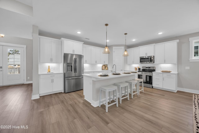 kitchen with appliances with stainless steel finishes, a kitchen breakfast bar, light countertops, decorative backsplash, and white cabinets
