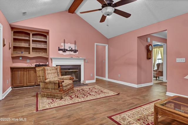 living room featuring wood finished floors, ceiling fan, a fireplace with flush hearth, a textured ceiling, and baseboards