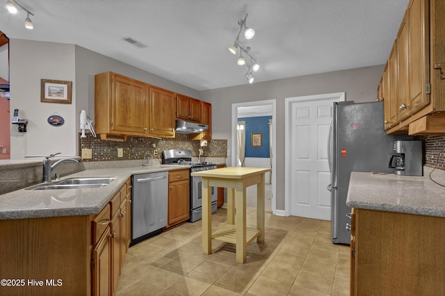 kitchen with appliances with stainless steel finishes, under cabinet range hood, a sink, decorative backsplash, and light tile patterned floors