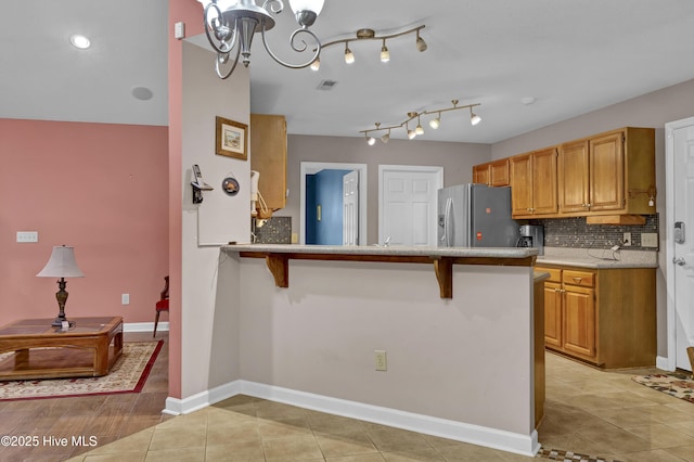 kitchen featuring stainless steel fridge with ice dispenser, decorative backsplash, a breakfast bar, a peninsula, and light countertops