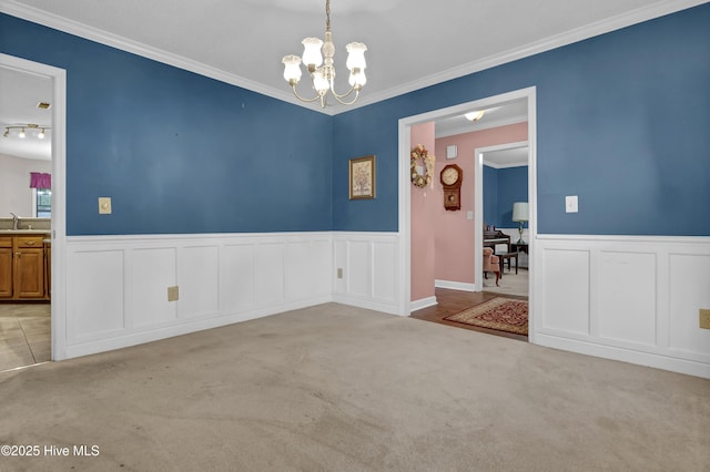empty room featuring a chandelier, carpet floors, a wainscoted wall, crown molding, and a sink