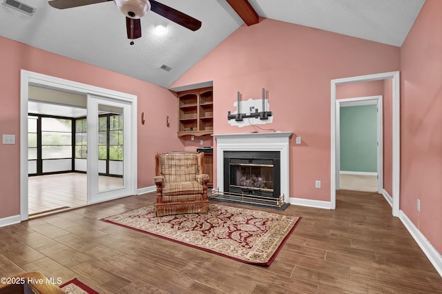 living area featuring a ceiling fan, a glass covered fireplace, wood finished floors, beam ceiling, and baseboards