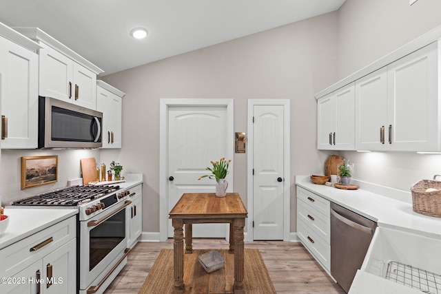 kitchen with stainless steel appliances, light wood-style flooring, lofted ceiling, white cabinetry, and light countertops