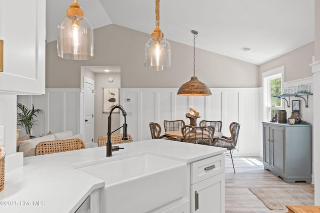 kitchen featuring a sink, a decorative wall, lofted ceiling, white cabinetry, and light countertops