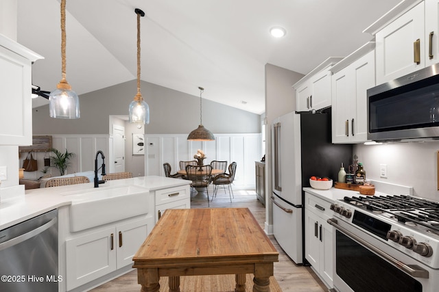 kitchen with appliances with stainless steel finishes, a sink, light countertops, white cabinets, and lofted ceiling