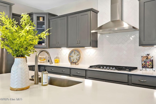 kitchen with wall chimney exhaust hood, gray cabinets, stainless steel gas cooktop, and a sink