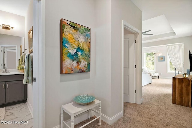 corridor featuring baseboards, light colored carpet, and a sink