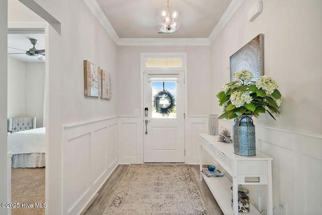 foyer featuring crown molding, wainscoting, a decorative wall, ceiling fan, and a chandelier