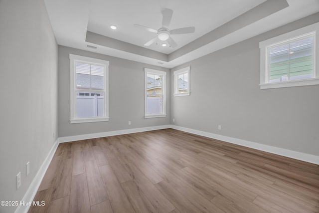 unfurnished room with a tray ceiling, wood finished floors, plenty of natural light, and recessed lighting