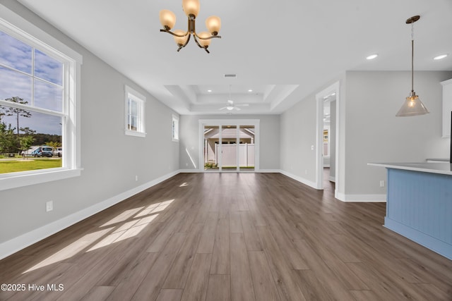 unfurnished living room with recessed lighting, a raised ceiling, a chandelier, wood finished floors, and baseboards