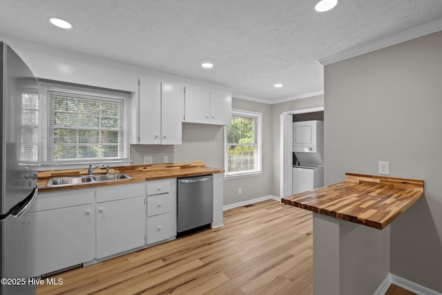 kitchen featuring stacked washer / dryer, butcher block countertops, stainless steel appliances, a sink, and baseboards