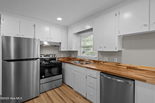 kitchen with stainless steel appliances, butcher block countertops, under cabinet range hood, a sink, and recessed lighting