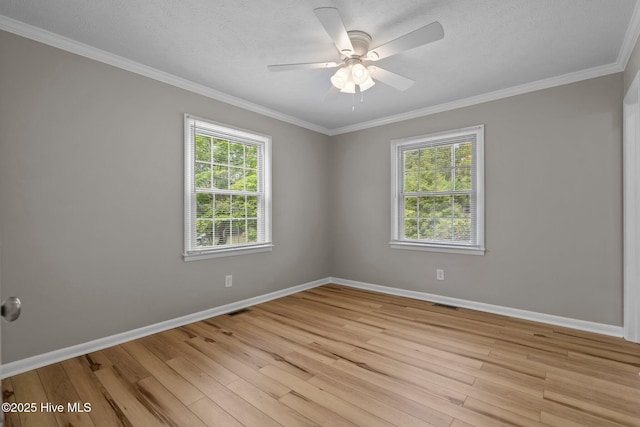 spare room featuring plenty of natural light, light wood finished floors, baseboards, ornamental molding, and a textured ceiling
