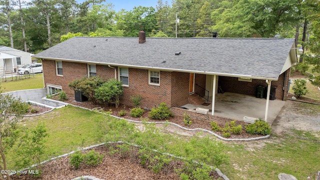 rear view of house featuring a shingled roof, brick siding, and a chimney