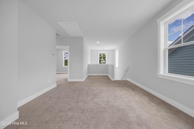 unfurnished room with attic access, carpet flooring, and baseboards