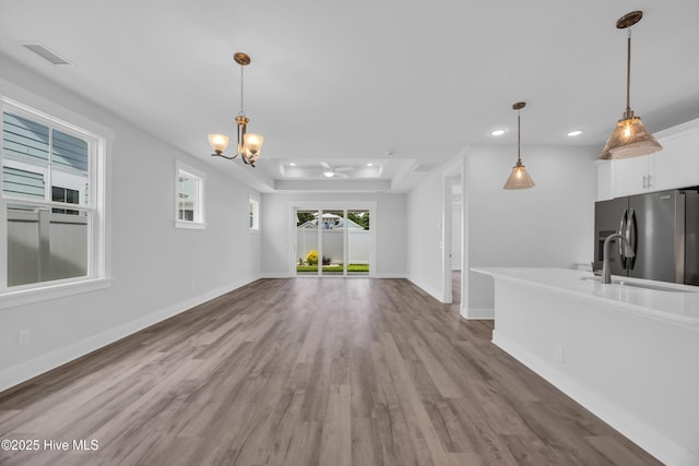 unfurnished living room featuring a tray ceiling, a chandelier, wood finished floors, recessed lighting, and baseboards