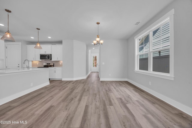 unfurnished living room with recessed lighting, light wood-style floors, a chandelier, and baseboards
