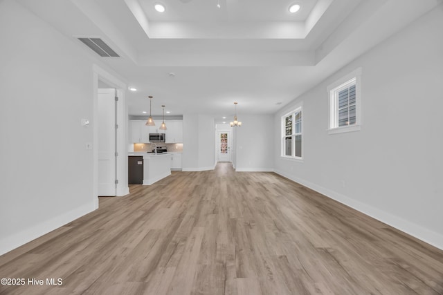 unfurnished living room featuring a chandelier, a raised ceiling, light wood finished floors, baseboards, and recessed lighting