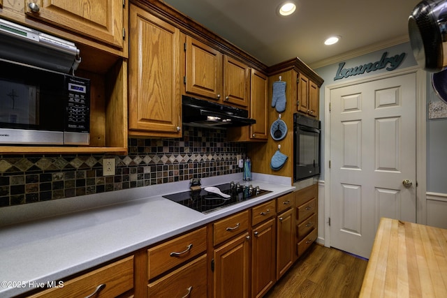 1992 Acorn Dr, New Bern, NC 28562 - kitchen featuring black appliances, under cabinet range hood, tasteful backsplash, dark wood-style flooring, and brown cabinetry