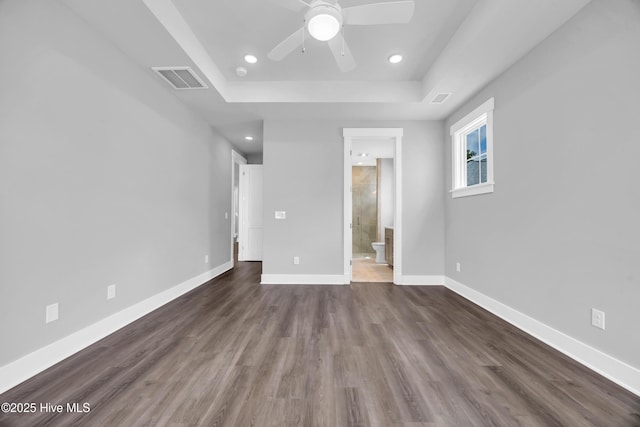 unfurnished bedroom with a tray ceiling, recessed lighting, dark wood-style floors, baseboards, and ensuite bathroom