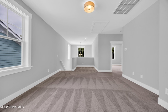 unfurnished living room with attic access, carpet, and baseboards