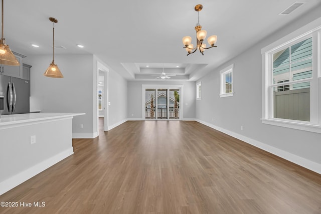 unfurnished living room featuring recessed lighting, a chandelier, wood finished floors, a tray ceiling, and ceiling fan