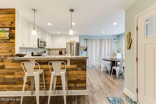 227 NE 38th St, Oak Island, NC 28465 - kitchen with appliances with stainless steel finishes, light stone counters, white cabinetry, a breakfast bar area, and a peninsula