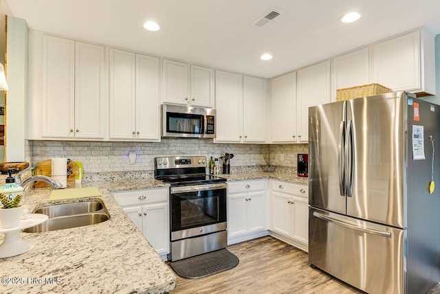 227 NE 38th St, Oak Island, NC 28465 - kitchen with appliances with stainless steel finishes, white cabinets, light wood-style floors, tasteful backsplash, and recessed lighting