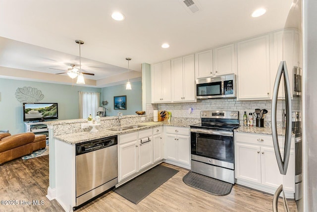 227 NE 38th St, Oak Island, NC 28465 - kitchen with stainless steel appliances, open floor plan, a peninsula, light wood finished floors, and white cabinetry