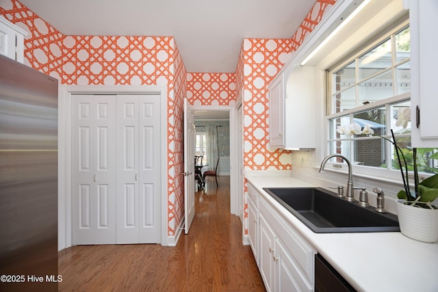 kitchen featuring a sink, wallpapered walls, wood finished floors, freestanding refrigerator, and white cabinets