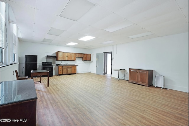 9291 NC-171, Williamston, NC 27892 - kitchen with radiator heating unit, black electric range oven, brown cabinetry, light wood finished floors, and a drop ceiling