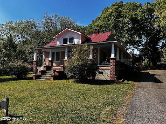view of front of house featuring a porch, a front lawn, metal roof, and driveway