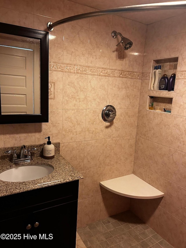 bathroom featuring a tile shower, vanity, and tile walls
