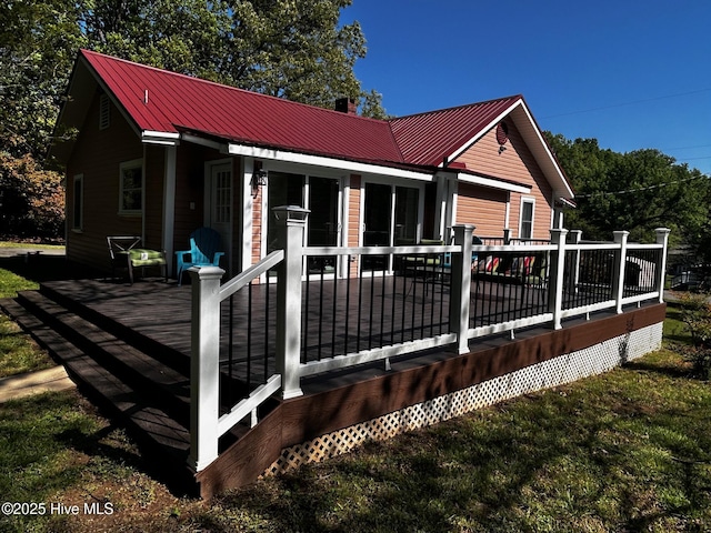 back of house featuring a deck, metal roof, a chimney, and a yard