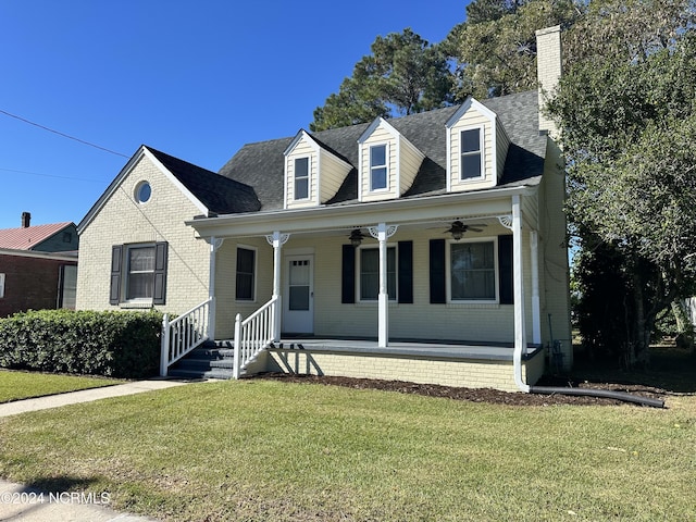 new england style home with a ceiling fan, a porch, a front yard, a chimney, and roof with shingles