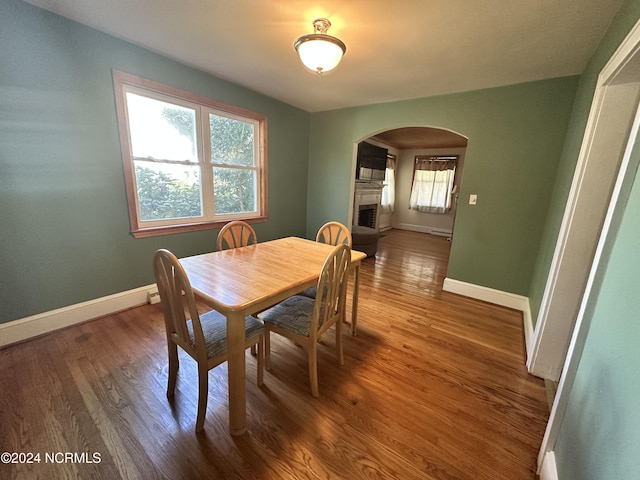 dining space with arched walkways, baseboards, wood finished floors, and a fireplace