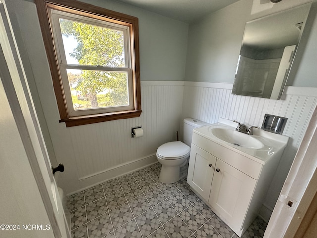 bathroom with wainscoting, toilet, vanity, baseboards, and tile patterned floors