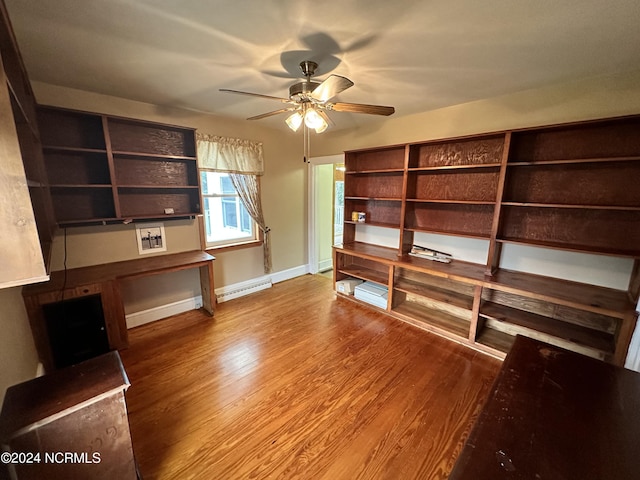 unfurnished office featuring baseboard heating, a ceiling fan, wood finished floors, and baseboards