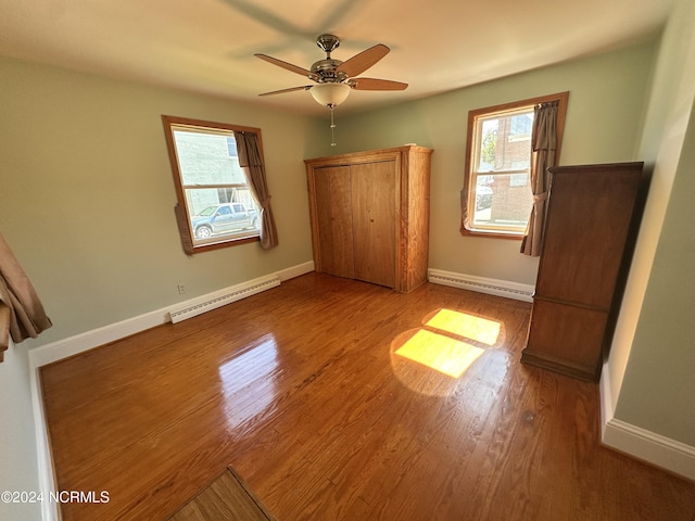 unfurnished bedroom featuring baseboard heating, wood finished floors, baseboards, and a ceiling fan