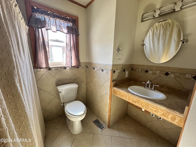 bathroom featuring a sink, toilet, tile patterned flooring, crown molding, and tile walls