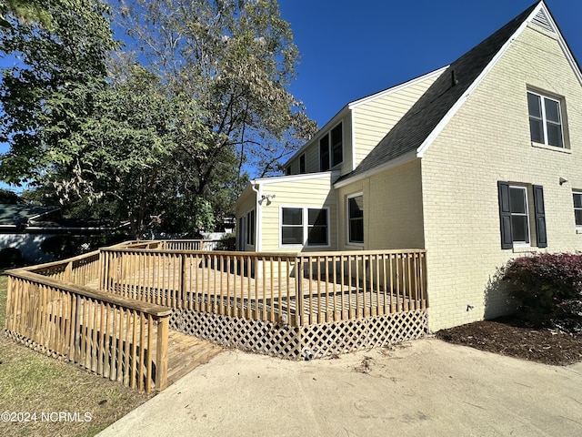 back of house with brick siding, a wooden deck, and roof with shingles