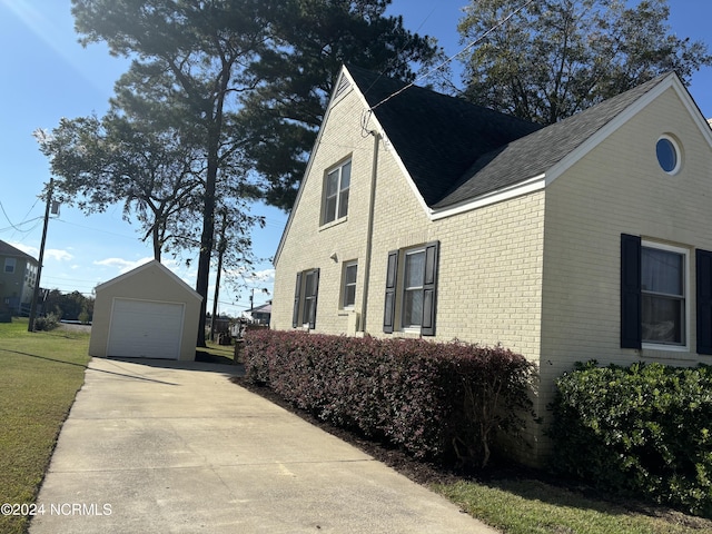 view of side of home featuring an outbuilding, brick siding, driveway, roof with shingles, and a detached garage