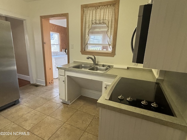 kitchen with a sink, washing machine and clothes dryer, freestanding refrigerator, black electric cooktop, and light countertops