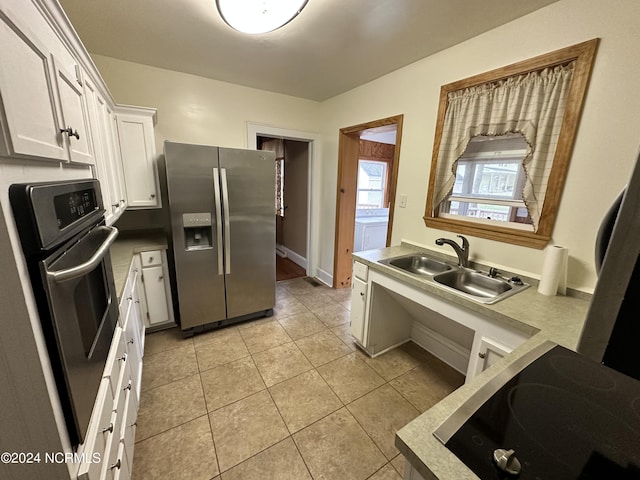 kitchen with appliances with stainless steel finishes, a sink, white cabinetry, light tile patterned flooring, and washer / clothes dryer